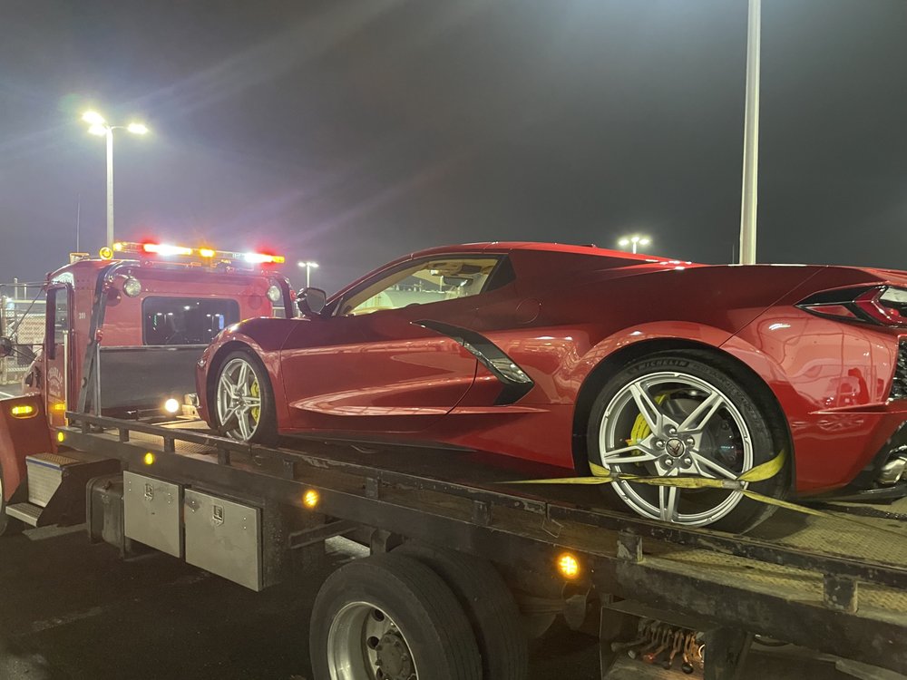 Red Corvette strapped down on a Charlie Towing flatbed under the lights