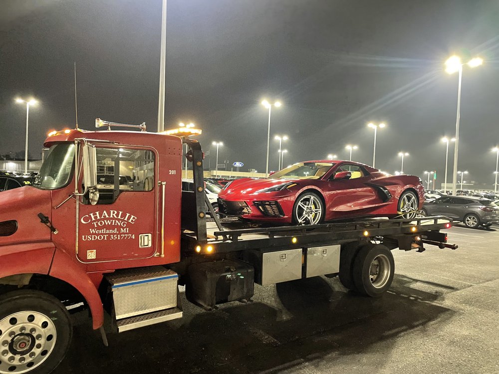 Charlie Towing flatbed loaded with a red Corvette at a dealership lot at night