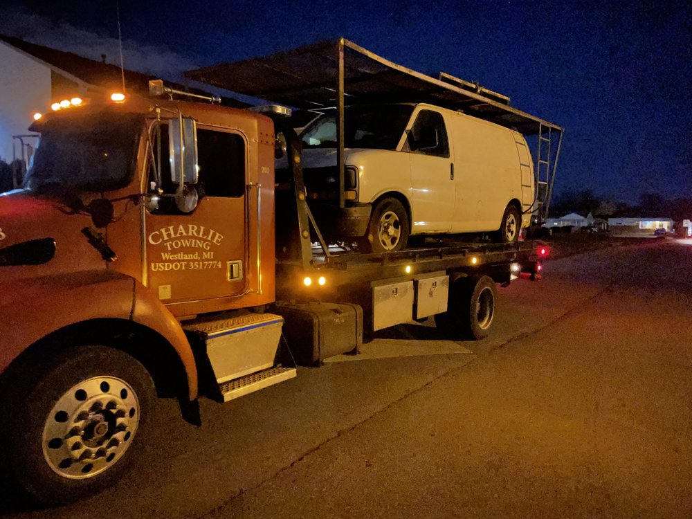 Charlie Towing truck transporting a cargo van on a residential street at night