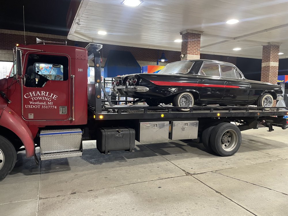 Black classic lowrider secured on a Charlie Towing flatbed at a gas station